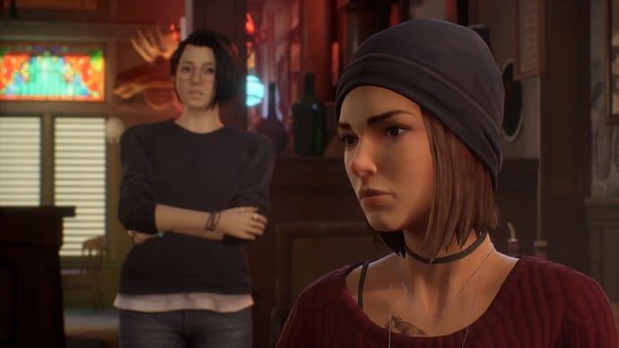 A screenshot from Life Is Strange: True Colors shows a scene from the Black Lantern tavern, with Steph sitting in the foreground and Alex standing a way behind her.