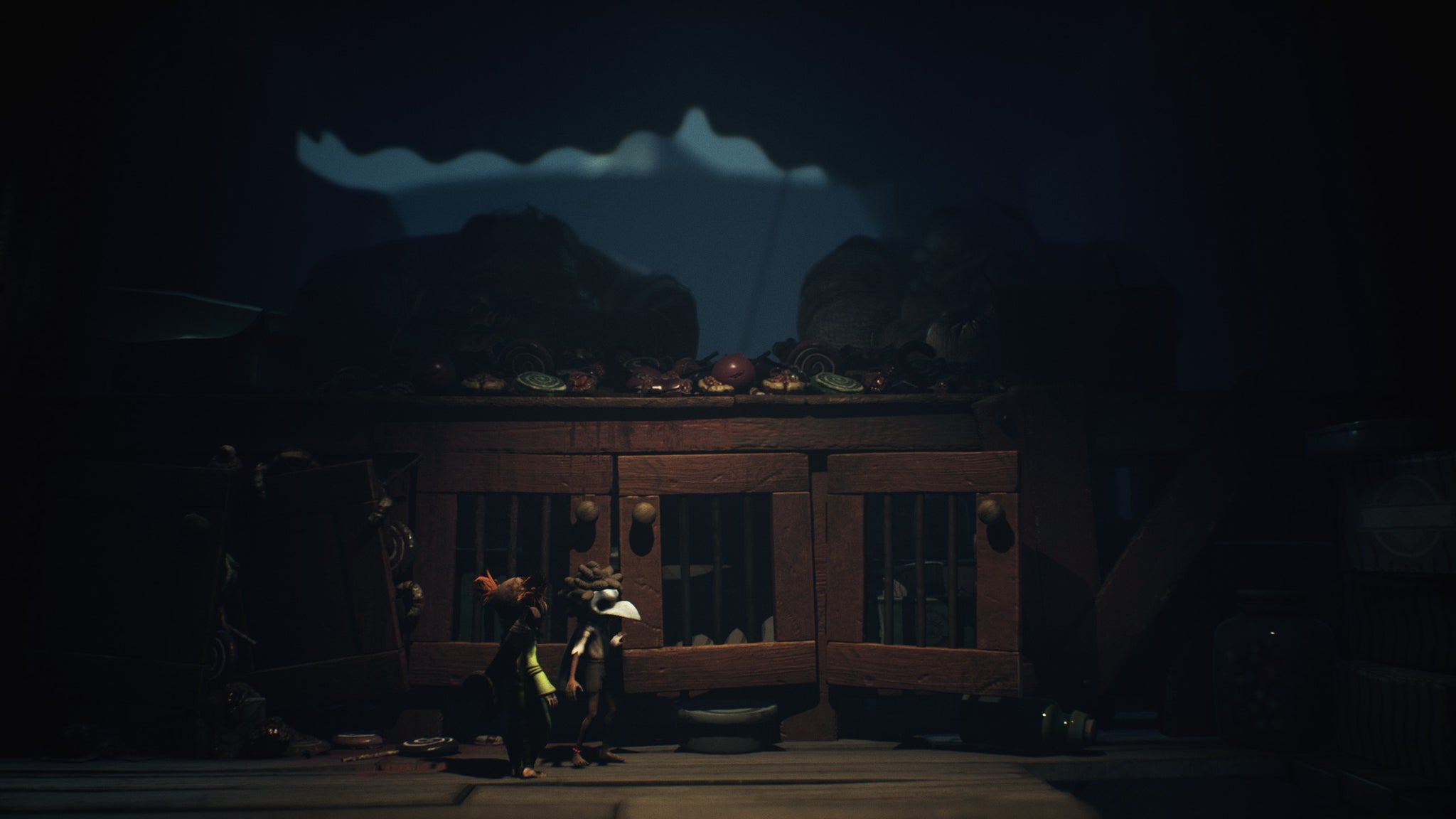 The stars of Little Nightmares 3 sneak by a table where large grotesque men eat. - 4