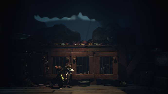 The stars of Little Nightmares 3 sneak by a table where large grotesque men eat.