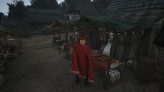 A man in a red cape and hat stands in front of a clothes stall in the marketplace of a town in Manor Lords