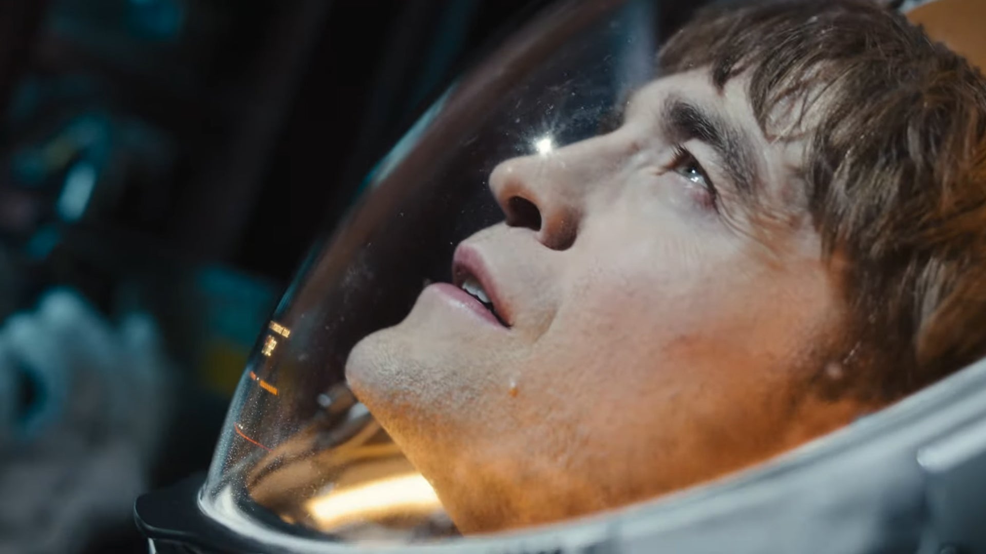 Robert Pattinson in Mickey 17, he's wearing a spacesuit looking out at something, eyes squinting slightly.