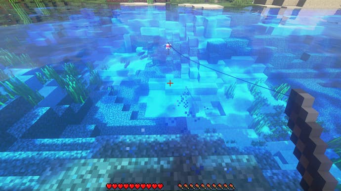 A player in Minecraft fishes in a lake. Between the bobber and the player, a v-shaped set of particles indicates the presence of a fish.