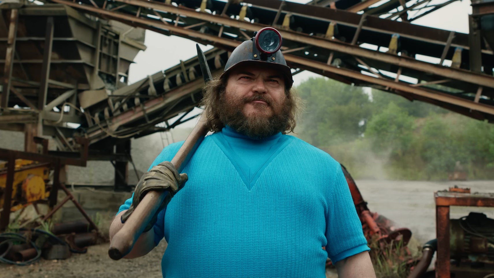 Jack Black is stood at a mining site, pickaxe in one hand, a helmet with a flashlight on his head in A Minecraft Movie. - 1