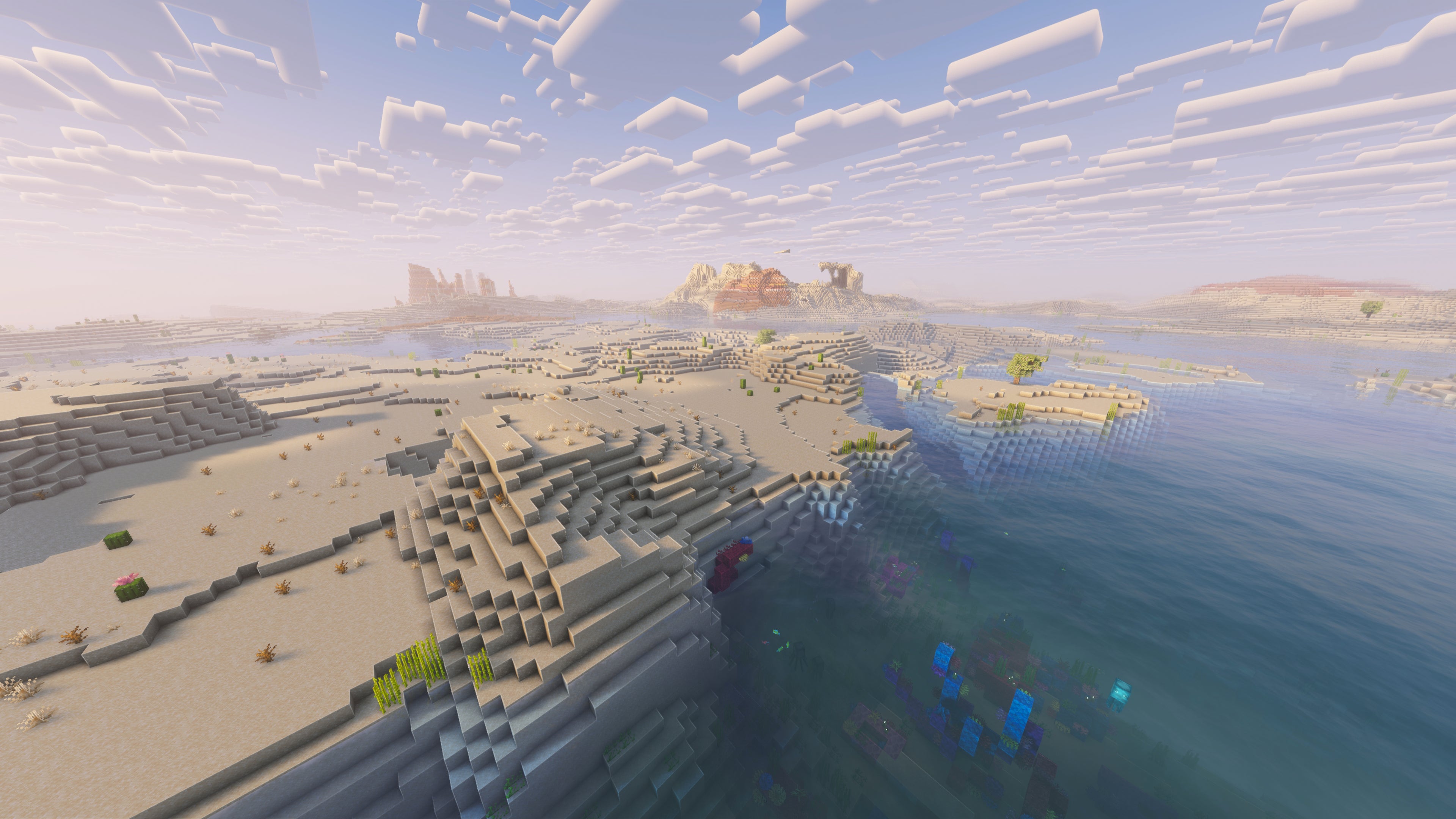 A landscape screenshot of a Minecraft seed, showing the edge of a Desert biome with a single tree, and Mesa hills in the distance. - 52