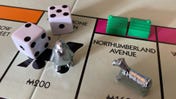 A pair of dice along with two silver player tokens on the Monopoly board, which also has two houses on Northumberland Avenue.