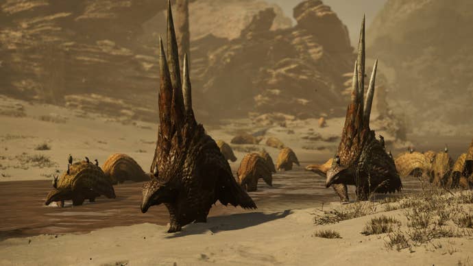 A Monster Hunter Wilds screenshot showing a herd of scaly creatures roaming through a desert as wind whips sand up around them.