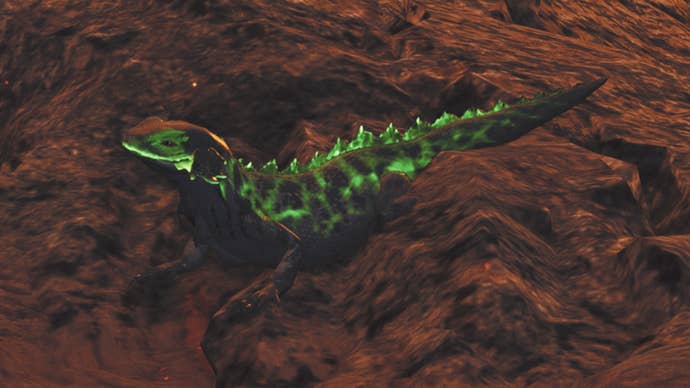 A close-up of an Ember Rufflizard in Monster Hunter Wilds, a small green lizard perched on some dark red rock in the Oilwell Basin.