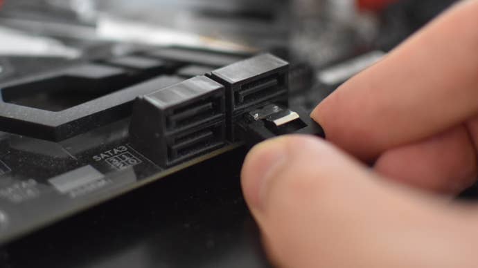 A SATA cable being connected by hand to a motherboard’s SATA port.