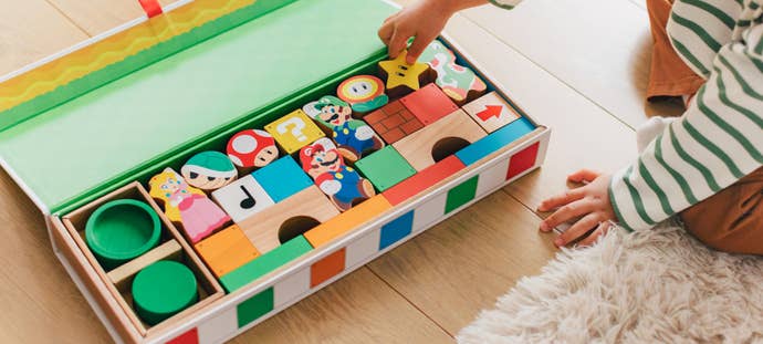 Promotional photo showing a young child reaching into a large box containing Mario-themed wooden blocks.