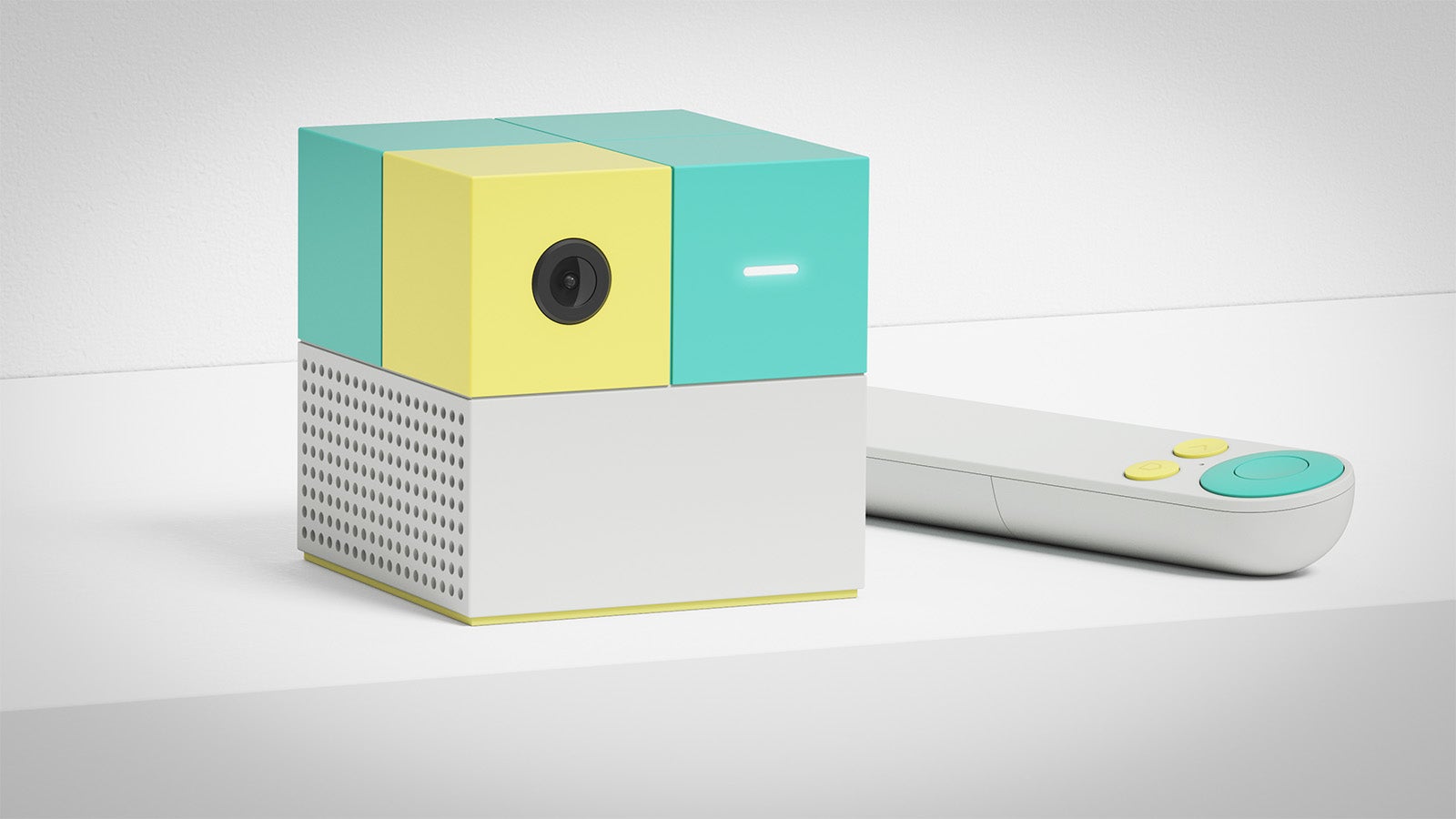 A cuboid games console with a separate controller. It's small - roughly palm-sized - and the bottom half is light grey while the top half is pale yellow and turquoise. A camera lens can be seen on the front of it. It's the Nex Playground machine.
