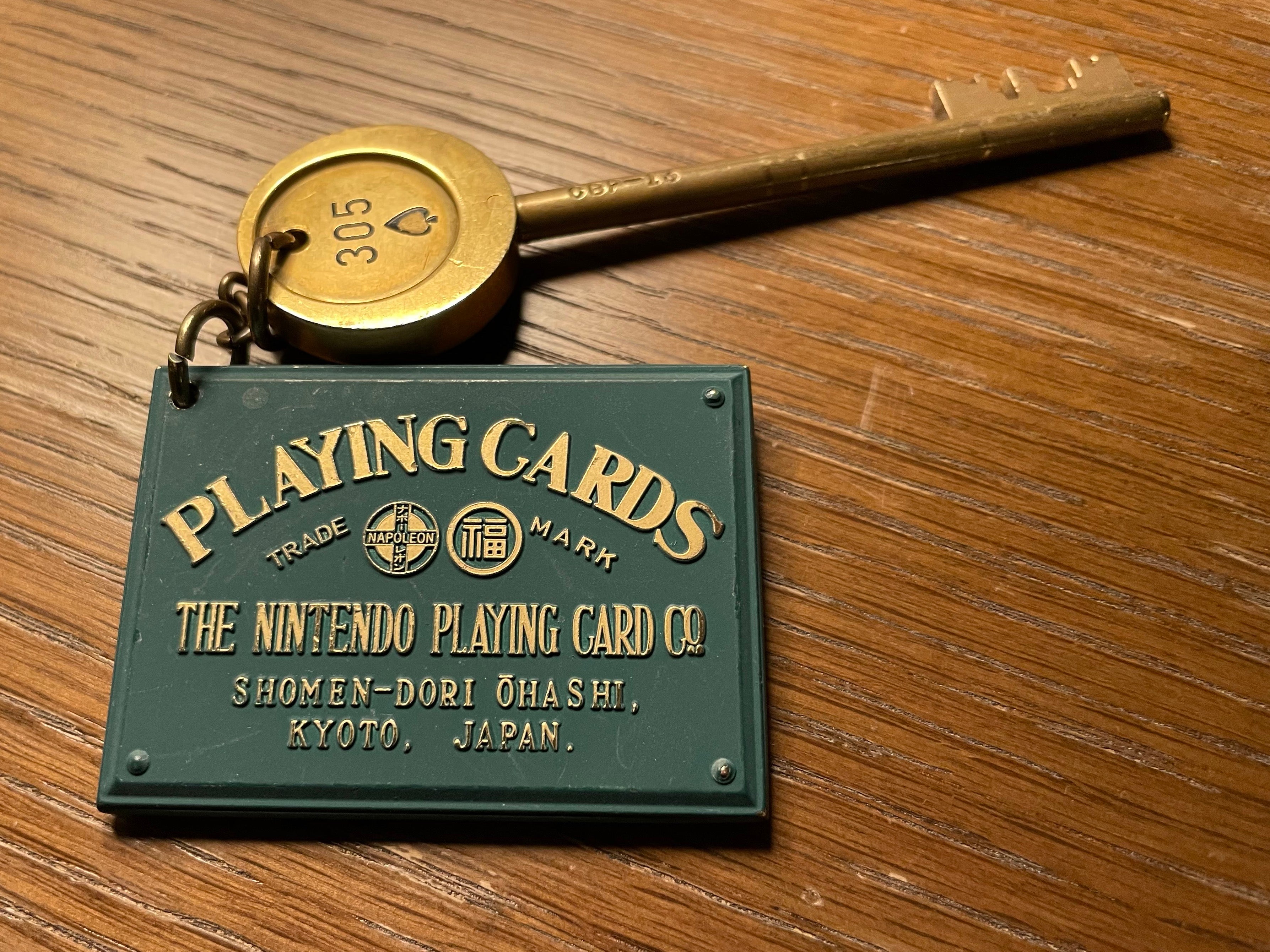 A Mortis key with a number on it, attached on a keyring to a green, card-sized rectangular metal plaque that reads &ldquo;Playing Cards&rdquo; by &ldquo;The Nintendo Playing Card Co.&rdquo;.