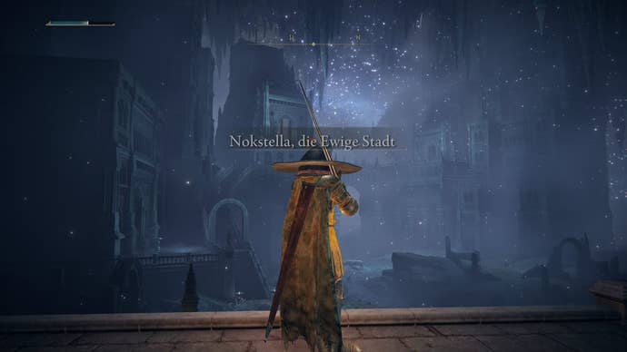 A warrior in Elden Ring stands in front of Nokstella, the Eternal City’s entrance, showing gothic buildings with a deep blue starry sky above