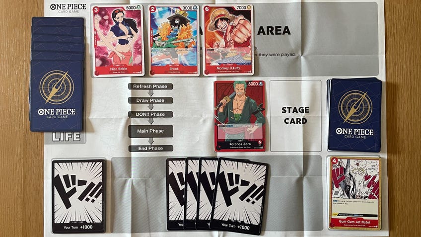 The starting setup for the One Piece Card Game, showing cards in their correct positions on the official play mat.