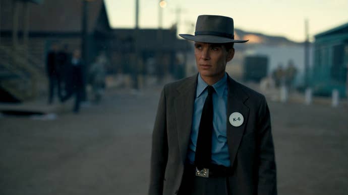 Cillian Murphy in Oppenheimer, he’s stood on a road, wearing a suit and a hat at sunset, he looks serious.