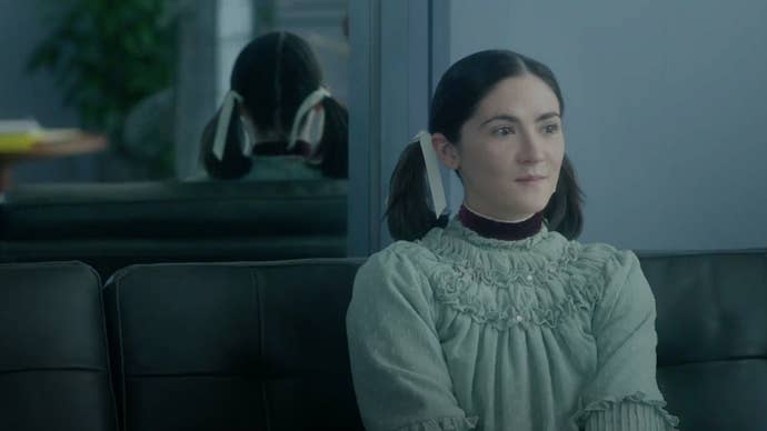 A woman with her hair in pigtails sat on a sofa in Orphan: First Kill.