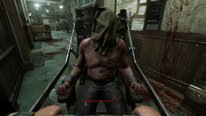 The Outlast Trails review screenshot, showing a man tied to a metal cart, a bag on his head and “SNITCH” carved over his heart