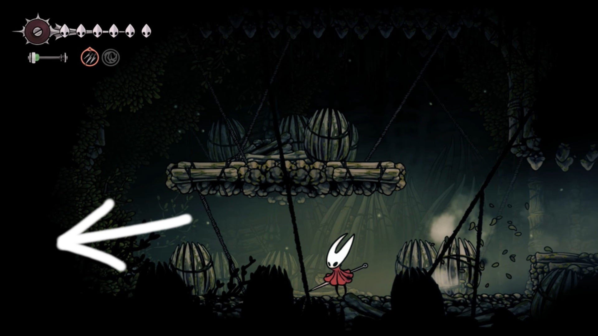 Hornet stands in a room of Hunter's March in Hollow Knight: Silksong; a large white arrow points to a wall that hides the secret Mottled Skarr seller. - 6
