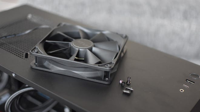 A PC case fan and its screws laying on top of an open case.