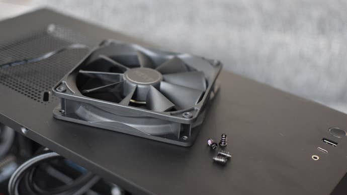 A PC case fan and its screws laying on top of an open case.