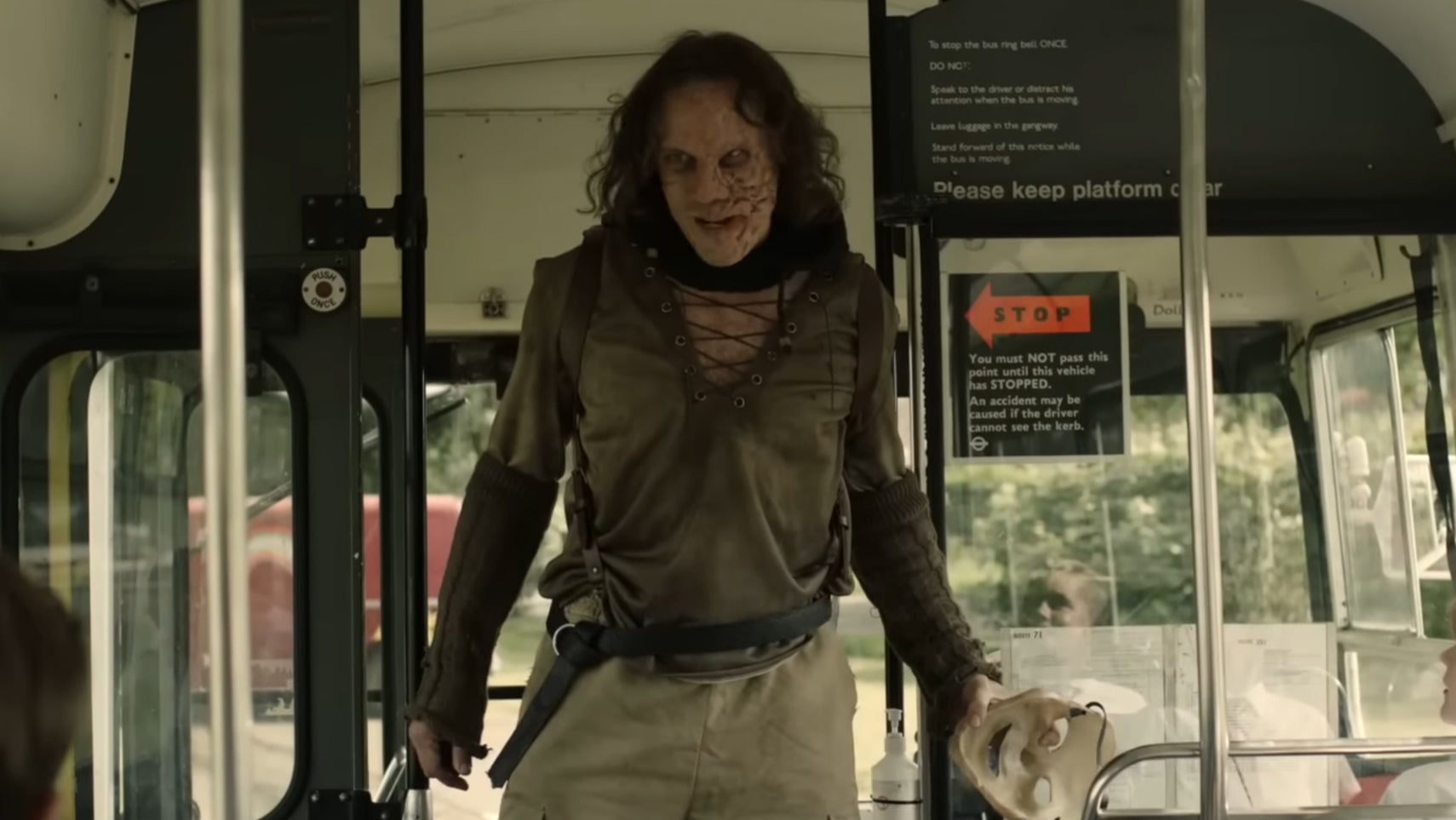 Still from Peter Pan's Neverland Nightmare, he is stood on a schoolbus looking menacingly at the offscreen children aboard it. - 1