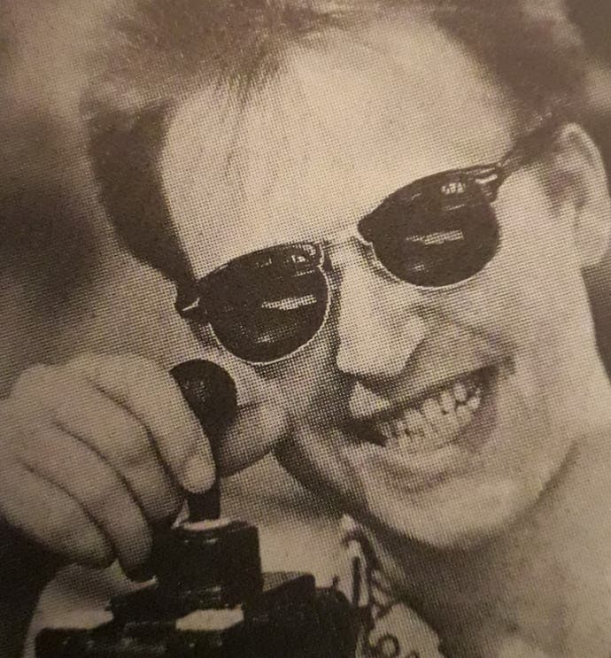 A portrait of Phil South, wearing hornrim sunglasses and holding a joystick