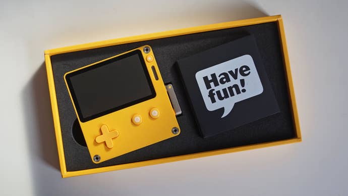 The Playdate inside its consumer packaging, with a cardboard USB wrapper saying ‘Have Fun!’ next to it