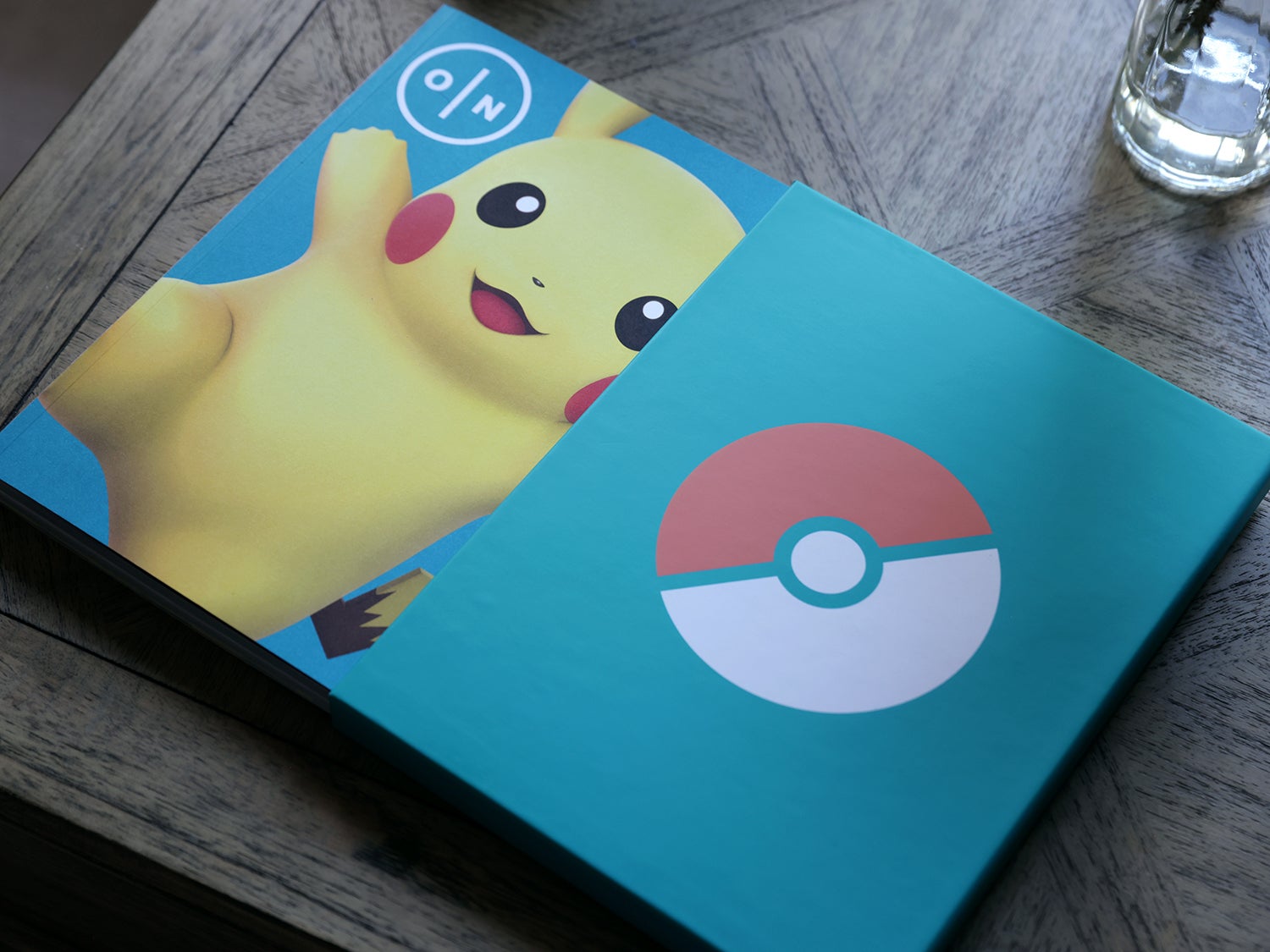 A photo of the coffee table journal ON Games Vol 2 on a table showing the Pokémon cover, a turquoise green with a Pikachu, and a Poké Ball themed slip case