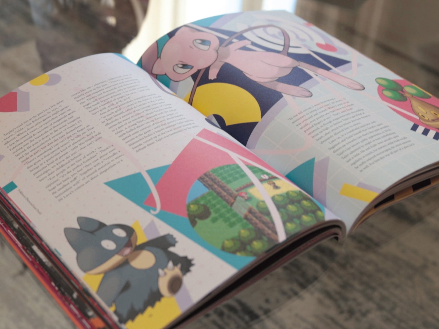 A photo of the coffee table journal ON Games Vol 2 on a table showing it open to a page showing Mew and Munchlax amongst the words of this story