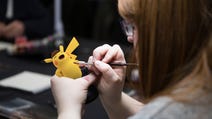 An over-the-shoulder photograph of a person with long hair painting a Warhammer miniature. Except, it's not a Warhammer miniature, it's cartoon Pikachu.