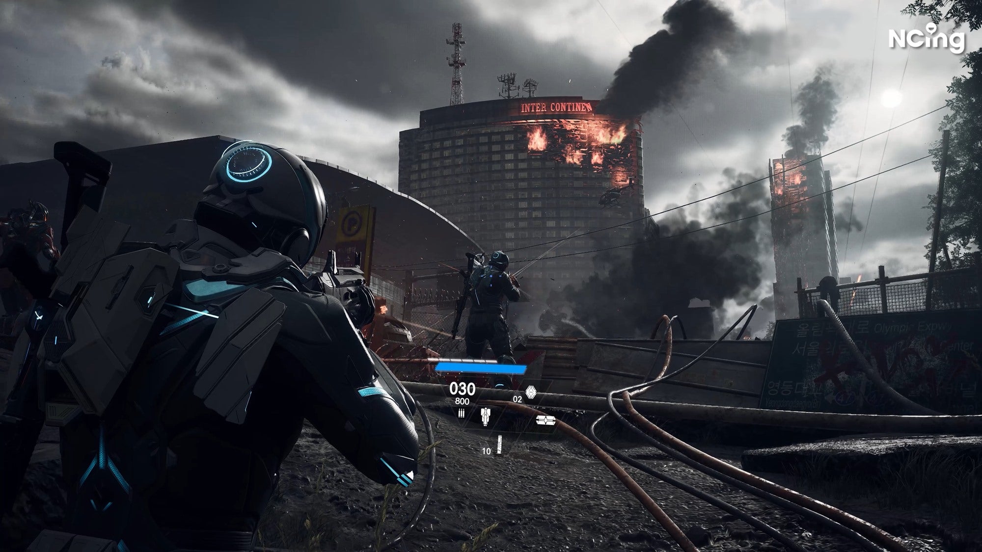 A sci-fi man points his gun at another sci-fi man as buildings burn in a grey modern world.