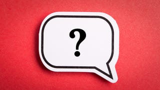 A photograph of a white paper speech bubble cut out and stuck on a red background. In the speech bubble is a black outline and a black question mark.