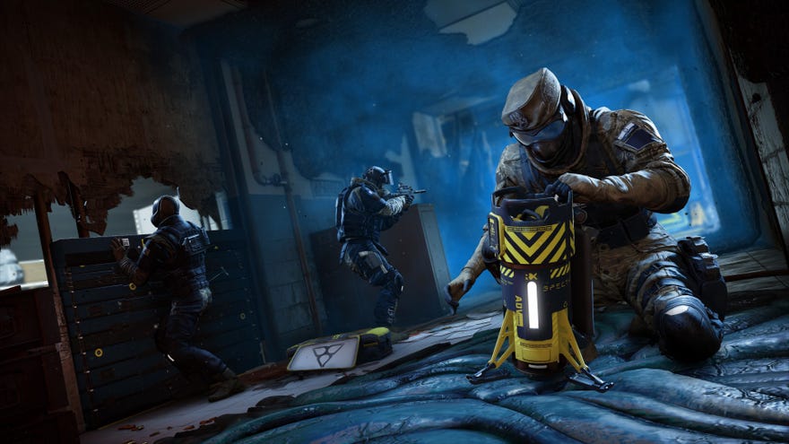 Operators set up defenses as another fiddles with a large canister in Rainbow Six Extraction.