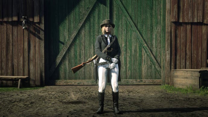 A lady stands in front of a stable, looking at the camera, in a long tailed black riding coat and white trousers and high black boots. And a black hat. She looks very smart.