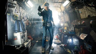 A young man is stood in a tech-filled caravan, he is wearing a VR headset while stood up, hand stretched out towards something in Ready Player One.