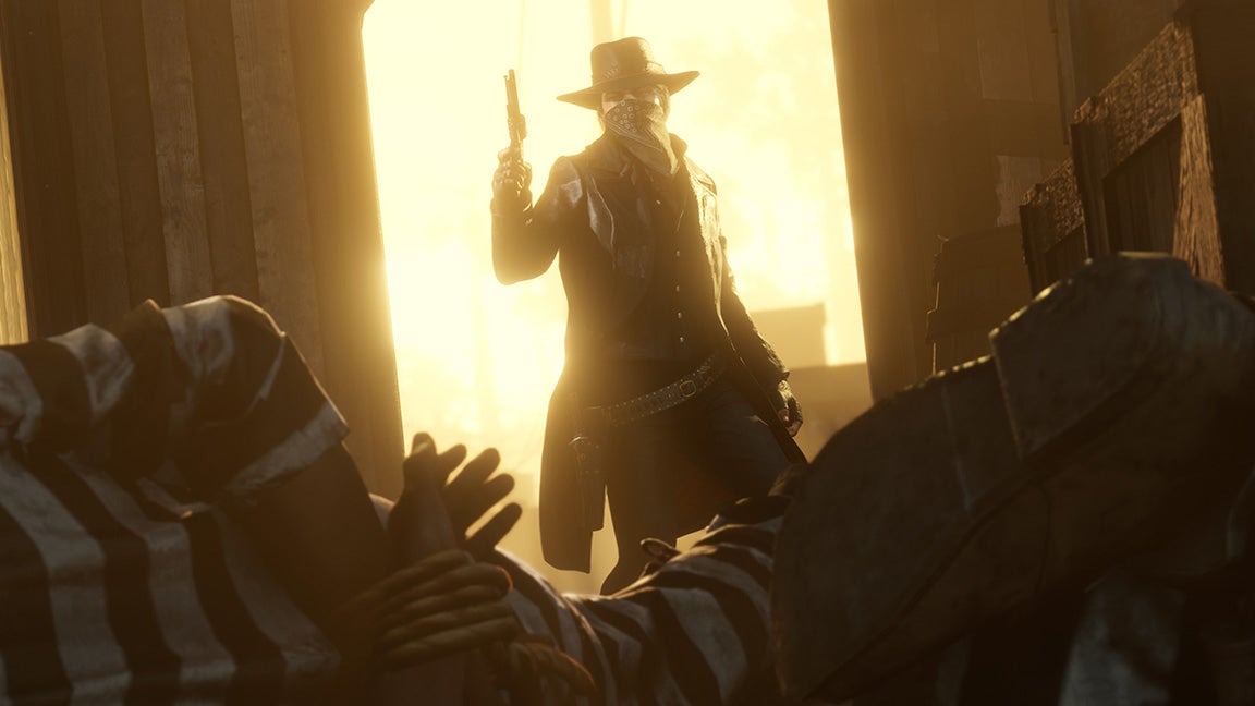 A Wild West character wearing a bandana over their face appears in a doorway holding a gun in Red Dead Redemption 2. - 1