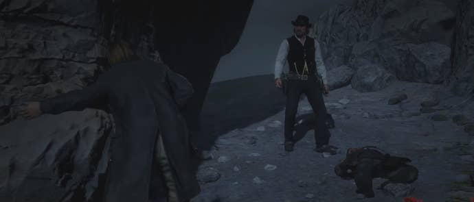Two Red Dead Redemption 2 characters stand in a darkly-lit, rocky region during the game's ending.