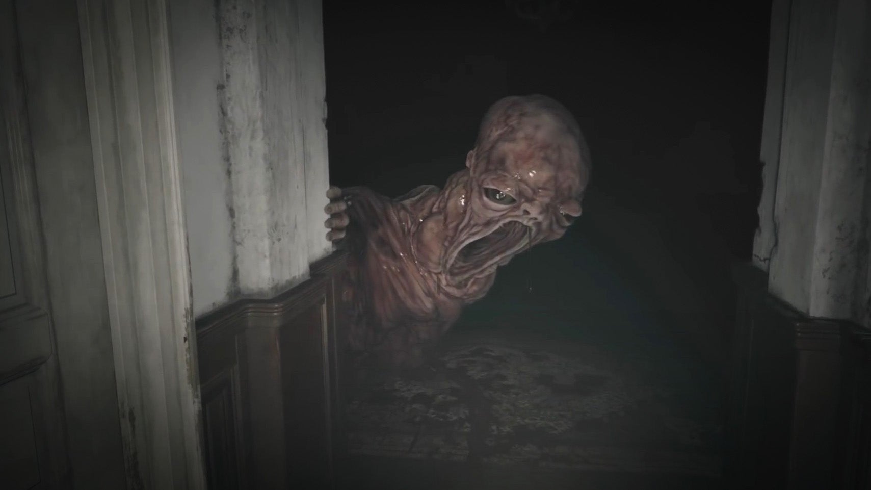 A huge, grotesque, disturbing baby monster flops around a dark hallway corner in Resident Evil Village.