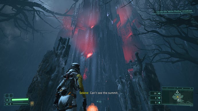 Selene stands in front of a giant, rocky fortress in Returnal. A red glow emits through the tower’s windows.