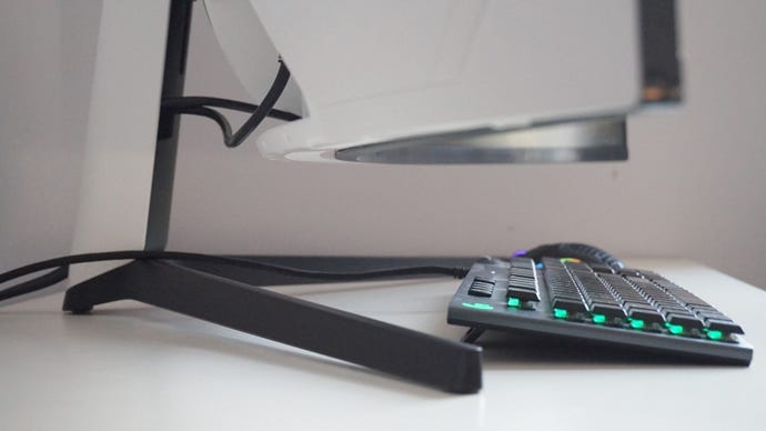 A photo of the Samsung Odyssey G9 gaming monitor’s stand from a side-on view, with a keyboard and mouse