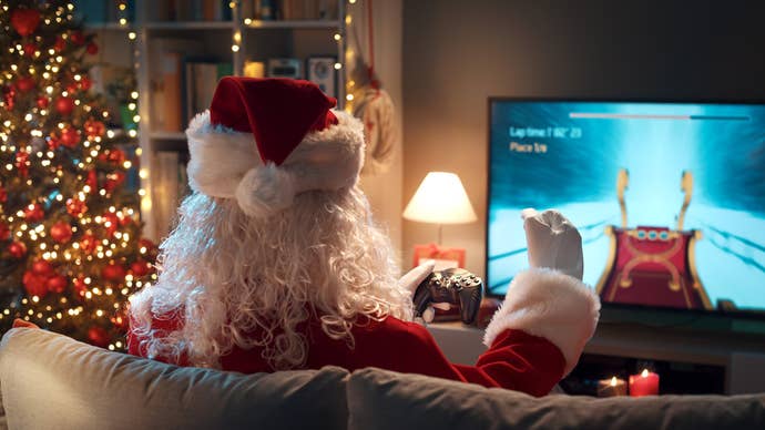 A photo looking in at a Christmas gaming scenario in a house, only, it’s Santa Claus we see the back of who is gaming on the TV. And they’re playing a sleigh-racing game. A Christmas tree shines brightly beside them.