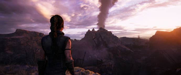 Senua looks at a distant smoke stack while walking in Senua’s Saga: Hellblade 2.