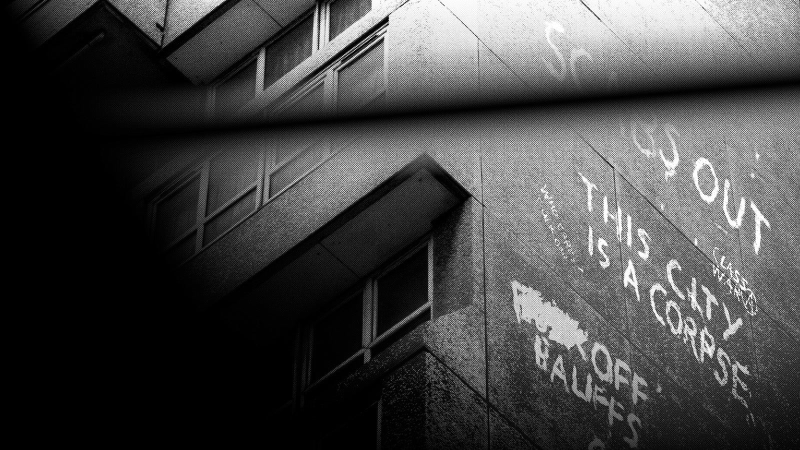 A black and white image showing the side of a block of flats with graffiti on. The words "this city is a corpse" can be clearly seen.