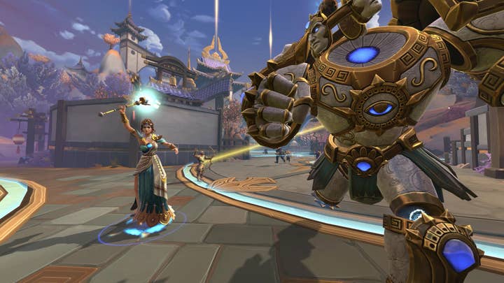 A Smite screenshot showing a woman holding a scepter aloft as a hulking construct with multiple detached faces on a ring where its head should be charges forward. In the background an archer lets loose a golden arrow