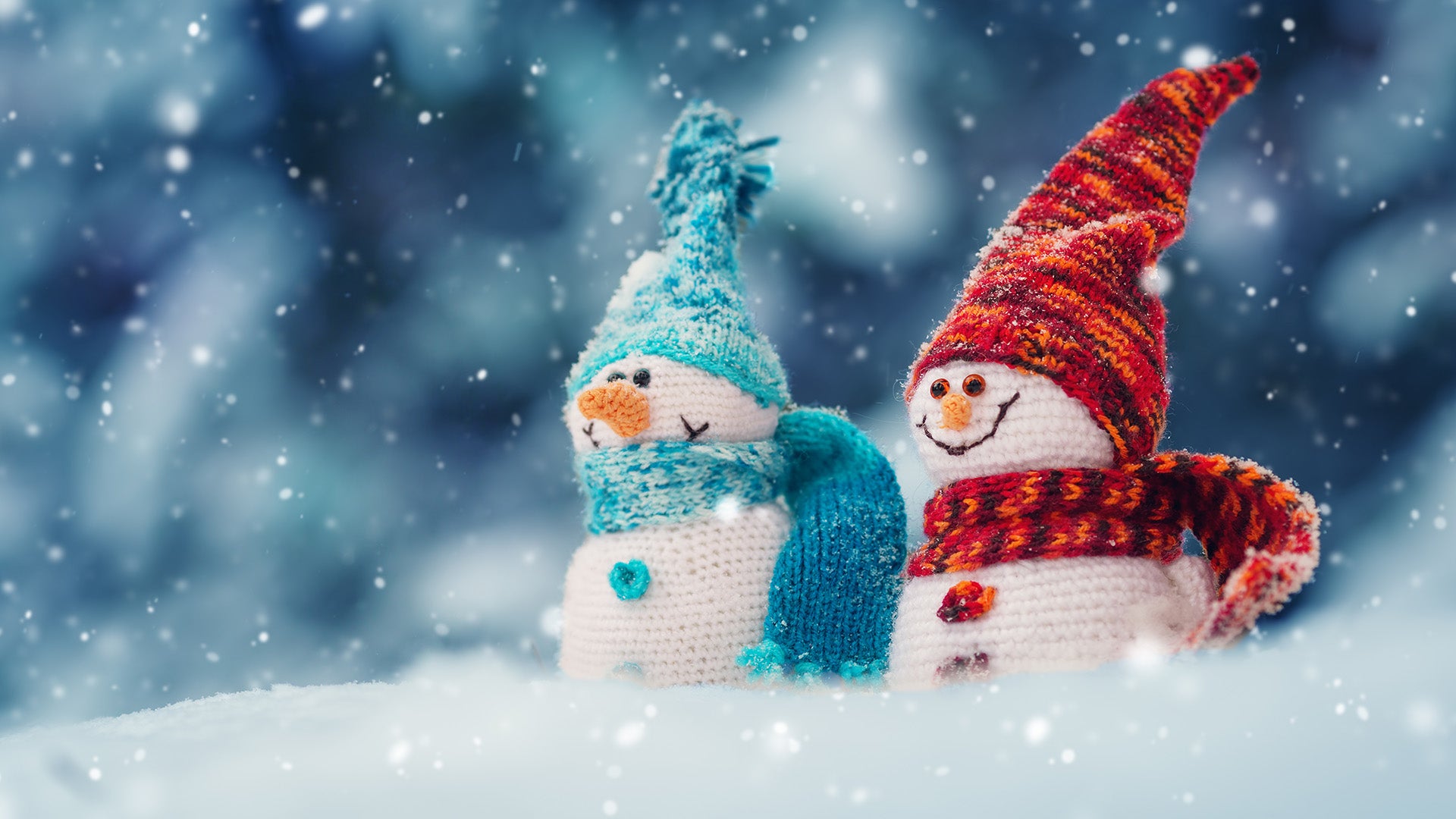 A photo of two small crocheted snowmen, who have big cheeky grins, standing in the snow.