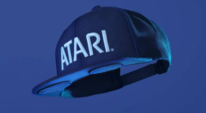 Promo image of Atari's Speakerhat, a baseball cap with the Atari logo on it and two circular bluetooth speakers jutting out of the underside of the brim