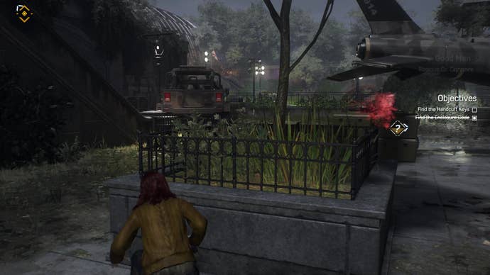 MJ hides behind a large square concrete planter with a helicopter in the background at the foot of a staircase with a jeep at the bottom.