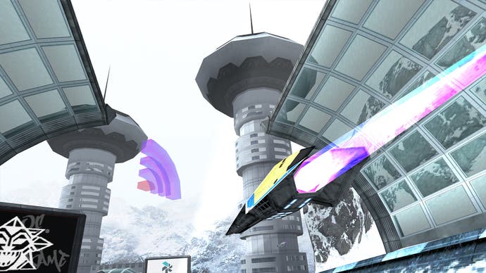 A screenshot of BallisticNG showing a futuristic low-polygon vehicle racing passed a covered spectator stand and heading toward two imposing towers.