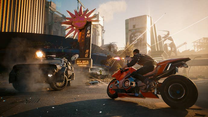 A screenshot from Cyberpunk 2077’s Phantom Liberty expansion showing the player racing through the city streets on a red motorcycle while an armoured vehicle opens fire up ahead.