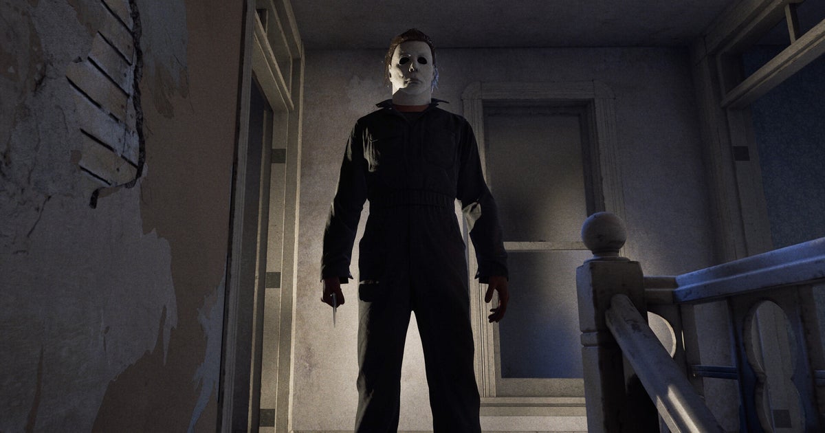 Photo: Gamesindustry A figure, Michael Myers, wearing a white mask and a dark jumpsuit stands in a dimly lit hallway, holding a knife