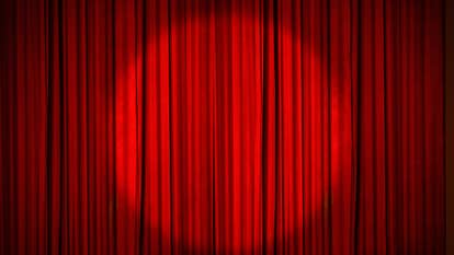 A red stage curtain, drawn, with a circular spotlight shining on the middle of it.